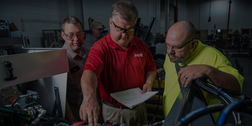 Three workers wearing safety glasses inspecting machinery in an industrial workshop.
